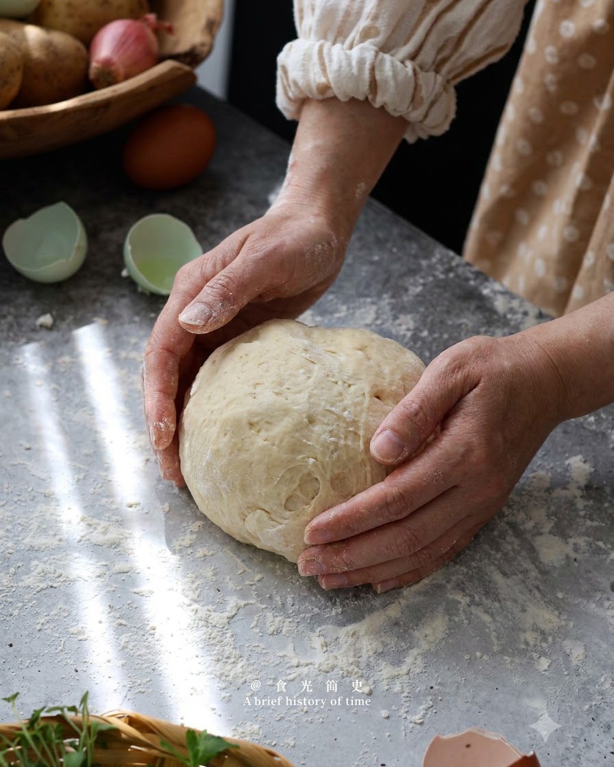 Manos formando y amasando suavemente la masa de ñoquis de patata hasta convertirla en una bola sobre una superficie enharinada.