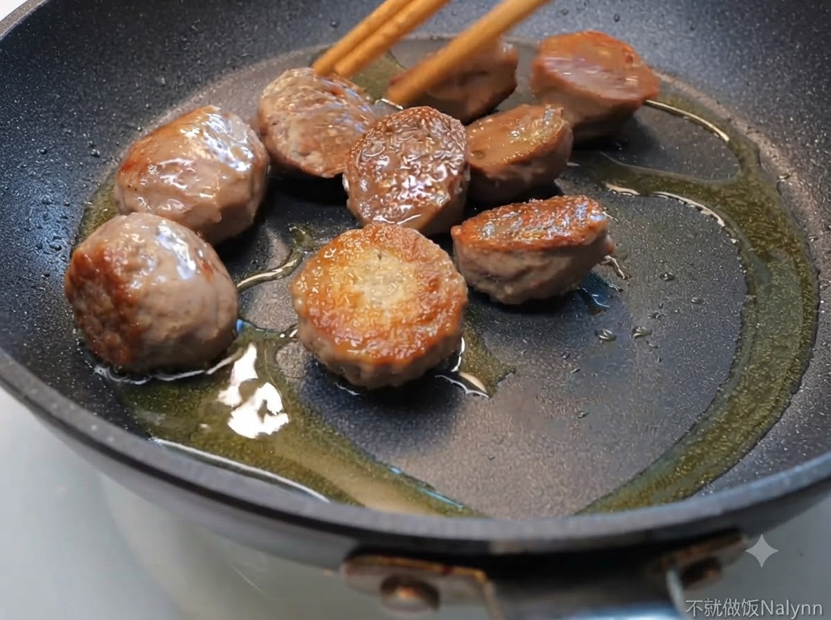 Mitades de albóndigas de ternera chisporroteando en una sartén con aceite, siendo movidas con palillos de madera.