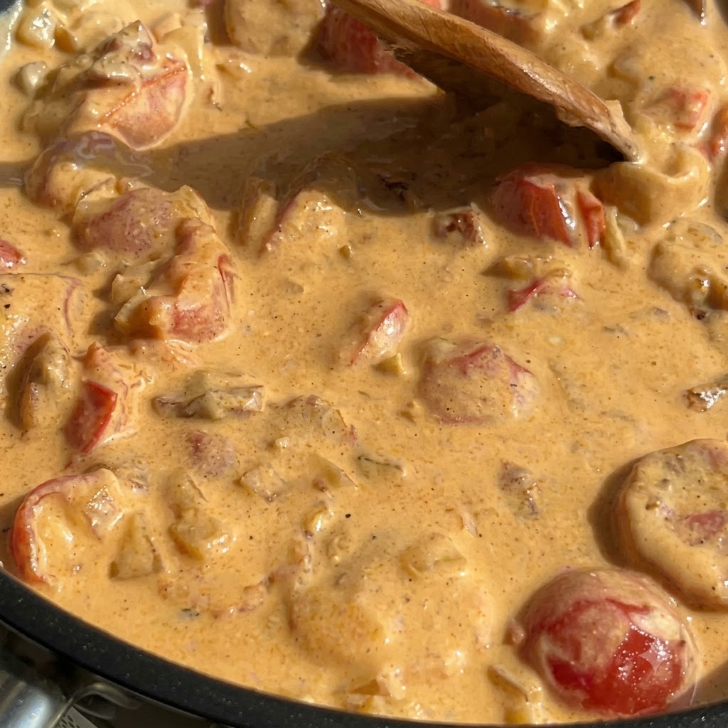 Pasta cocida, espinacas y salmón mezclados en una salsa cremosa espesa dentro de una sartén.