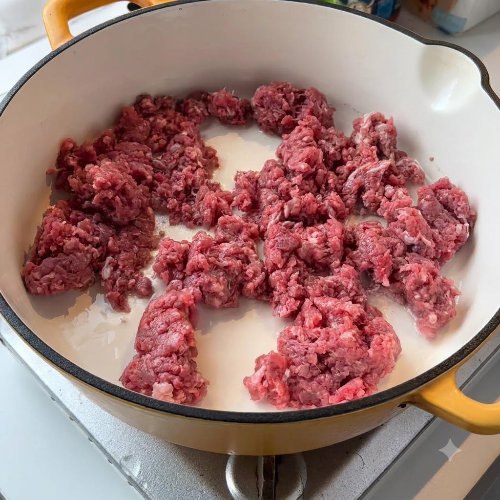 Carne picada de ternera cruda y cebollas blancas chisporroteando en una sartén de color claro en la estufa.