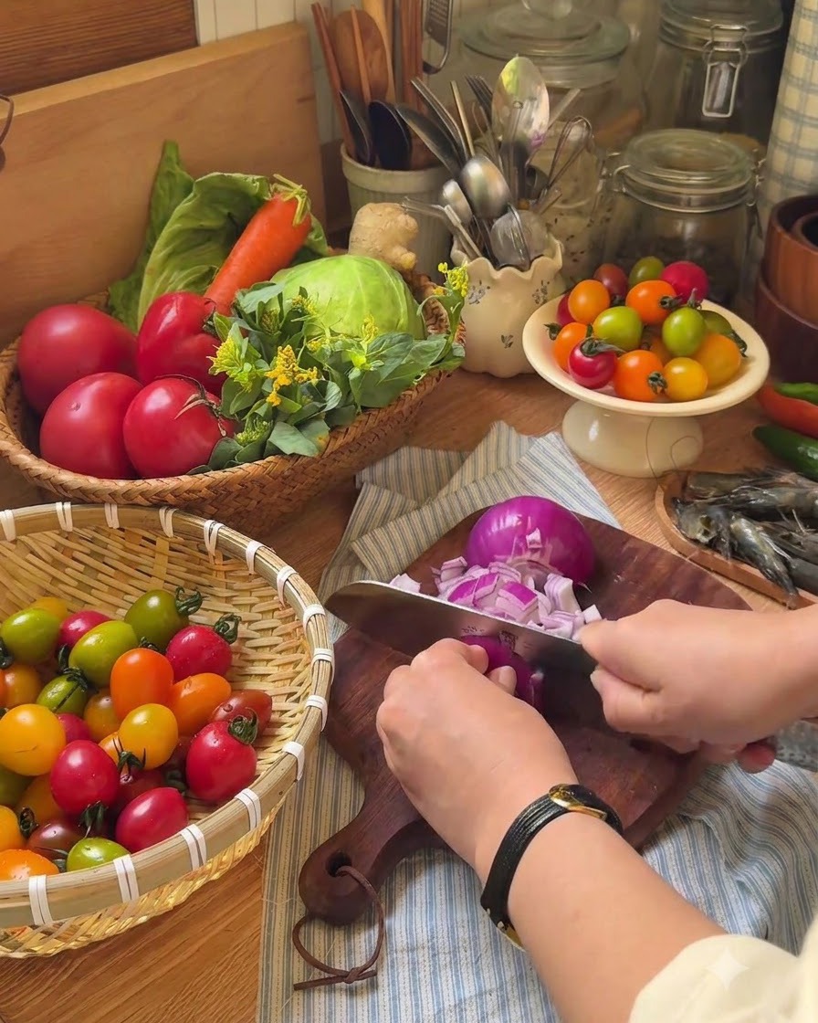 Una mano usando un cuchillo para cortar tomates cherry a la mitad en una tabla de cortar de madera.