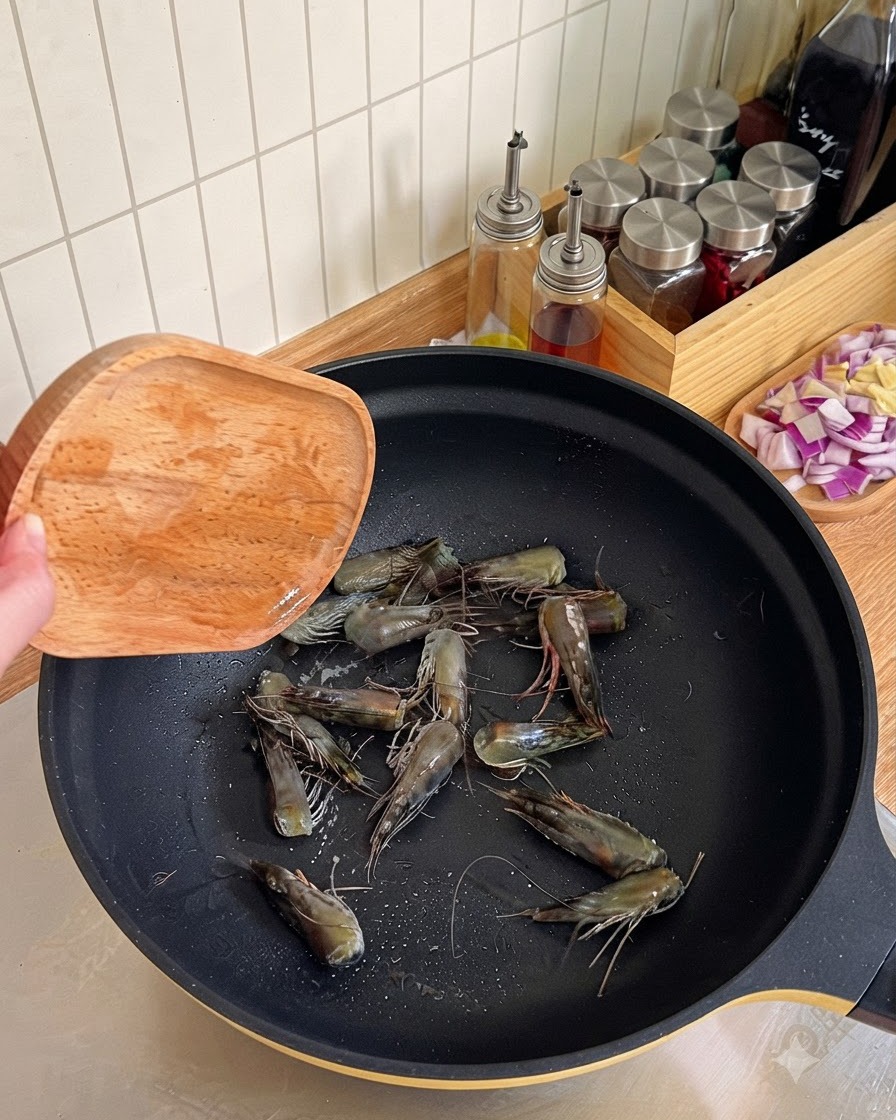 Cabezas de camarón siendo fritas y presionadas con una espátula de madera en un wok negro para extraer aceite.