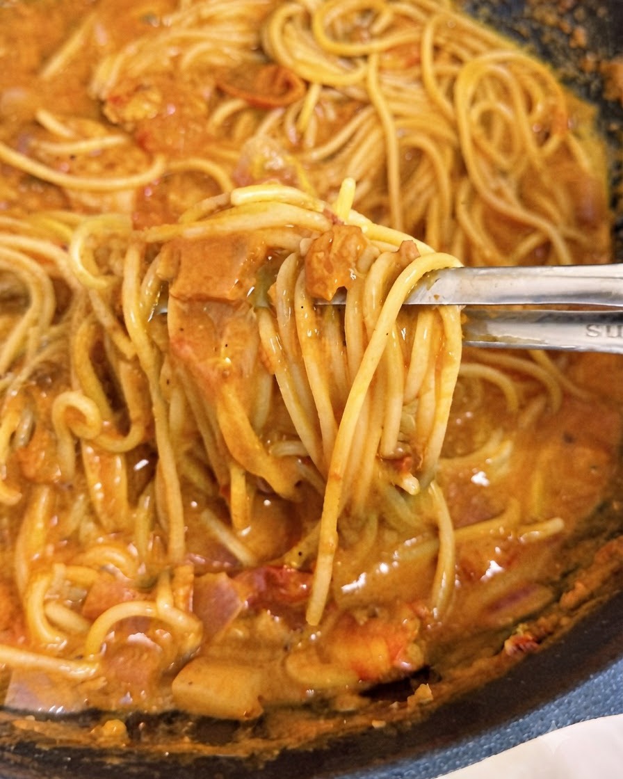Pinzas levantando hebras de espagueti cubiertas de salsa de tomate cremosa rosada dentro de un wok.