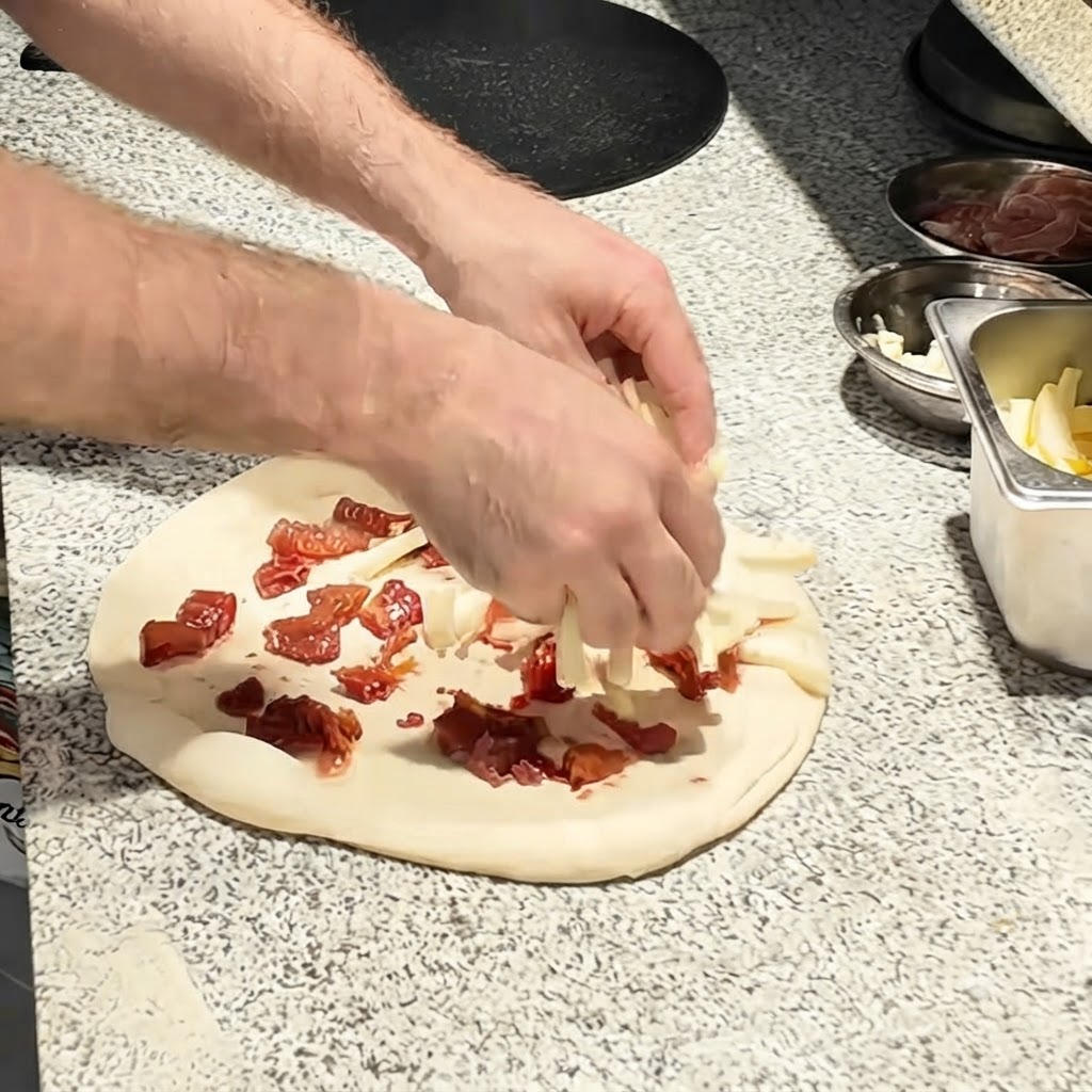 Tiras de queso mozzarella siendo espolvoreadas sobre la base de tomate en la masa de pizza.