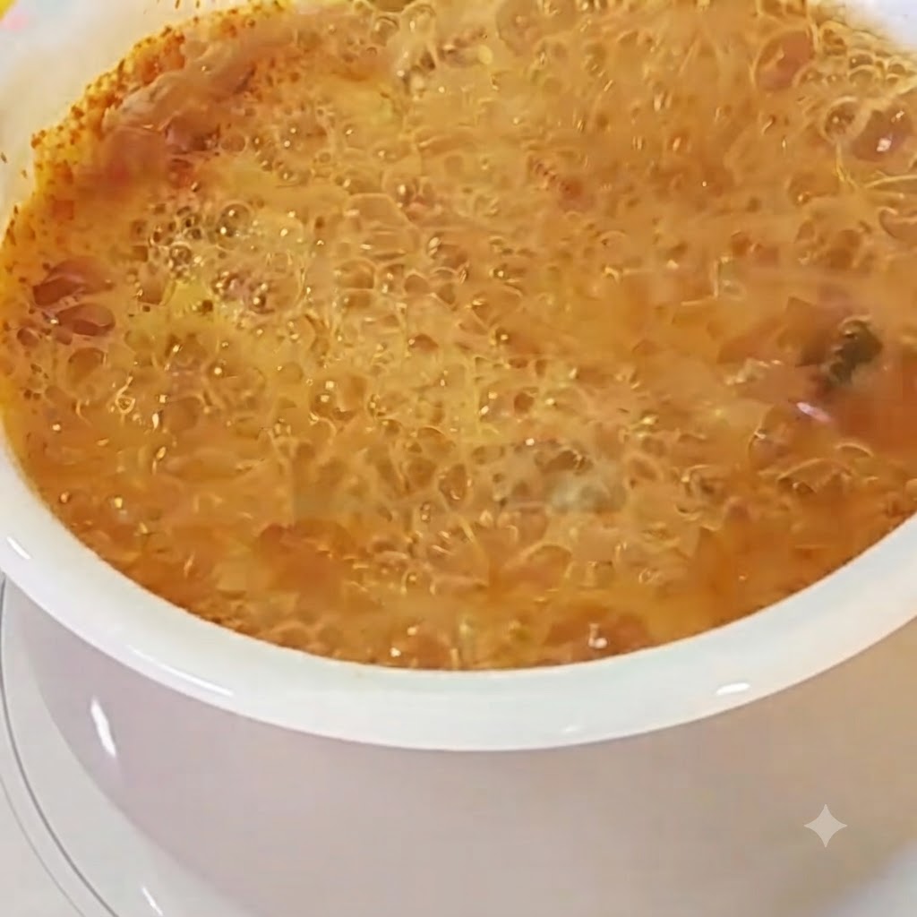 Un huevo cascado en una olla de caldo de ramen rojo burbujeante.