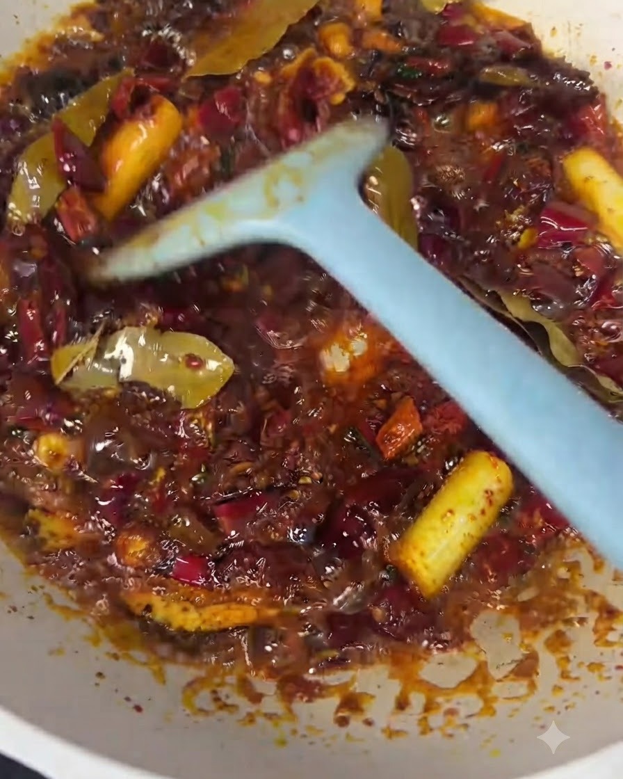Trozos de carne de ternera siendo mezclados en el aceite de chile rojo y la base de especias con una espátula azul.