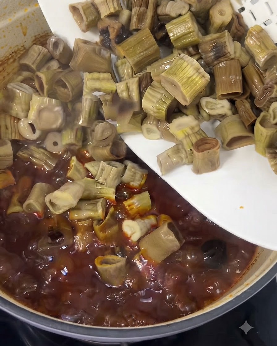 Brotes de bambú picados deslizándose desde un plato blanco hacia el estofado de ternera rojo burbujeante.