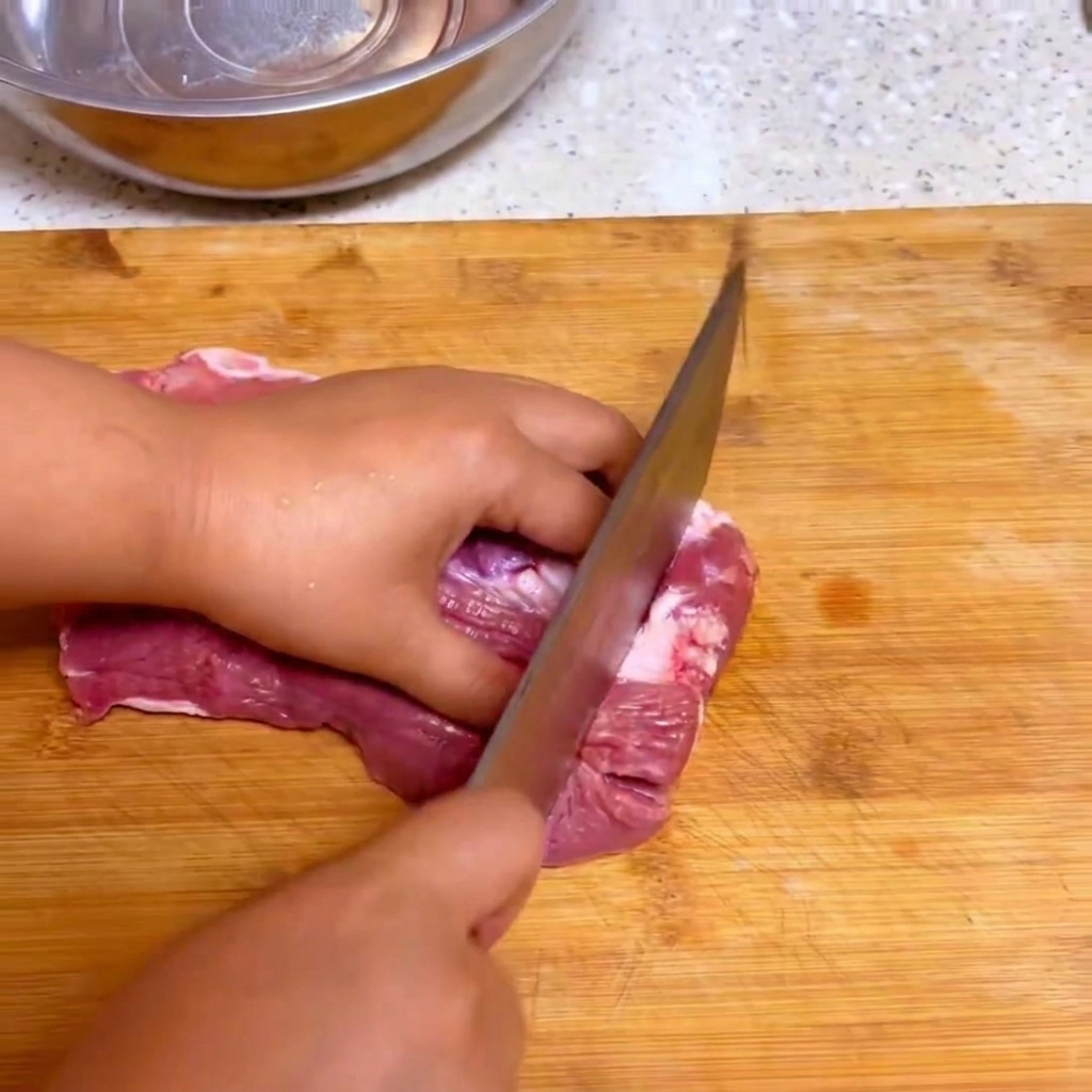Un cuchillo de cocina cortando carne de res fresca en trozos grandes sobre una tabla de cortar de madera.