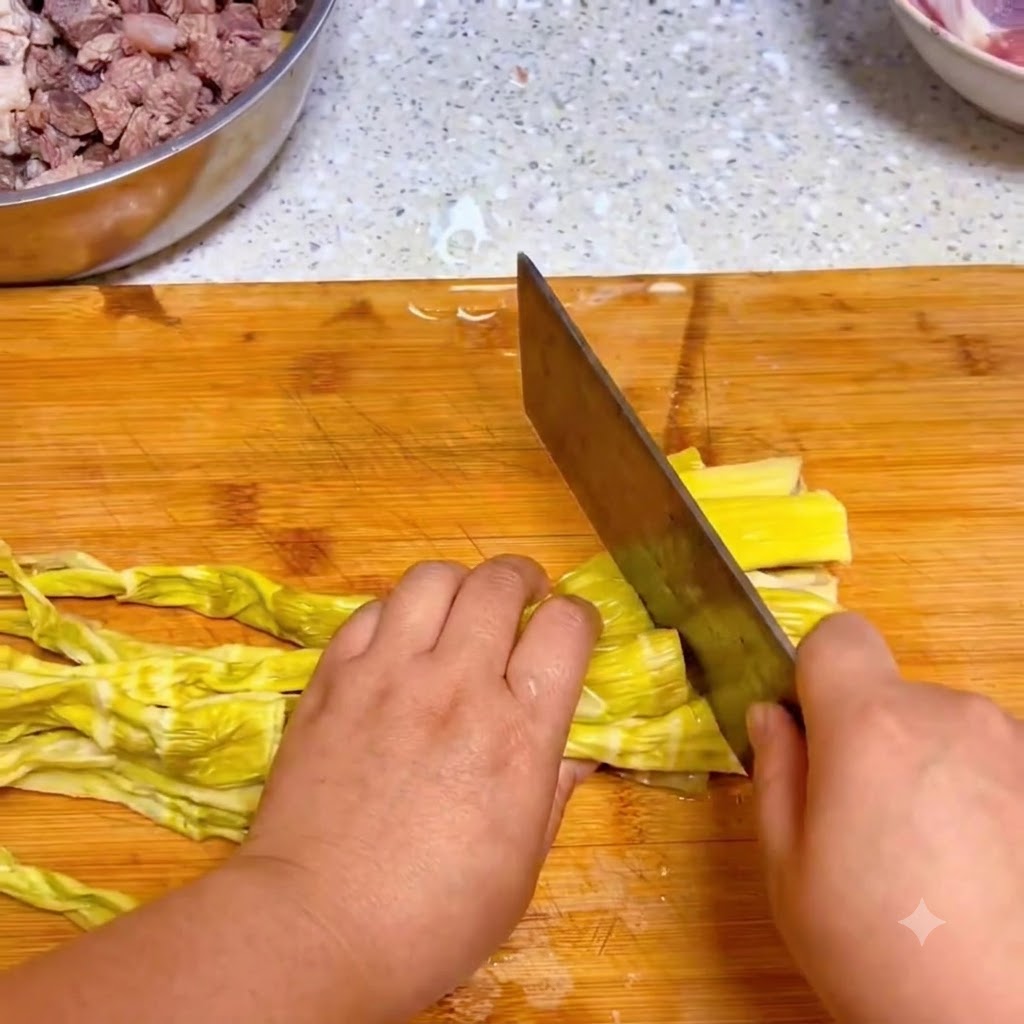 Un cuchillo de cocina cortando brotes de bambú amarillos rehidratados sobre una tabla de cortar de madera.