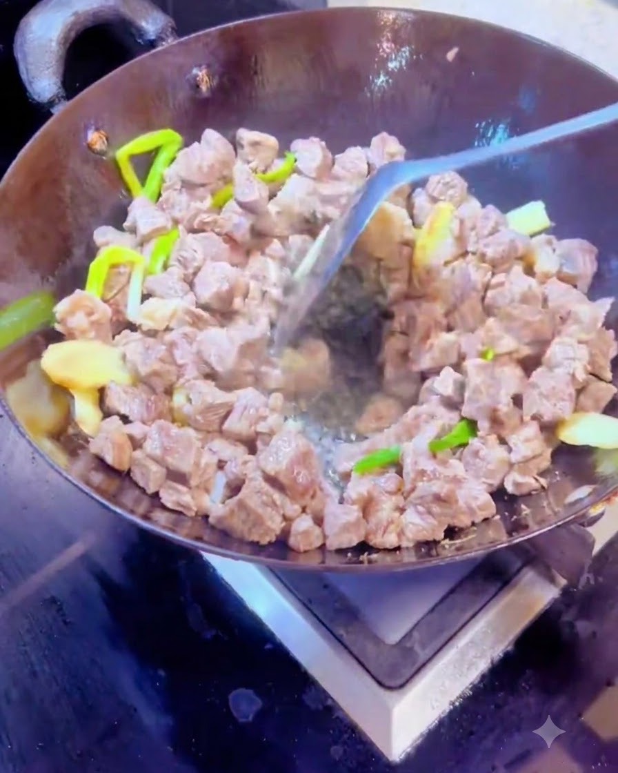Mezclando especias secas y cubos de carne juntos en un wok caliente usando una espátula de metal.