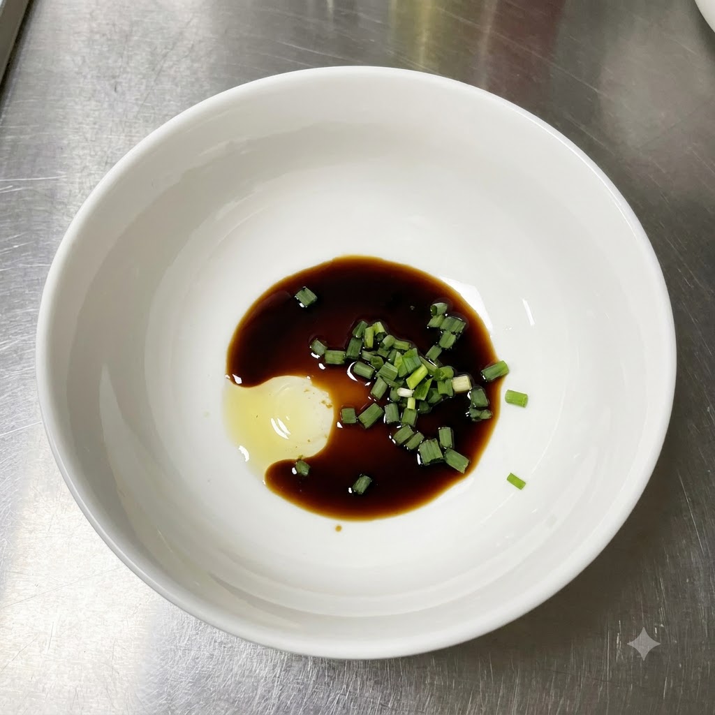Un bol blanco que contiene salsa de soja ligera, cebollinos verdes picados frescos y una porción de pasta de condimento en un mostrador de acero inoxidable.