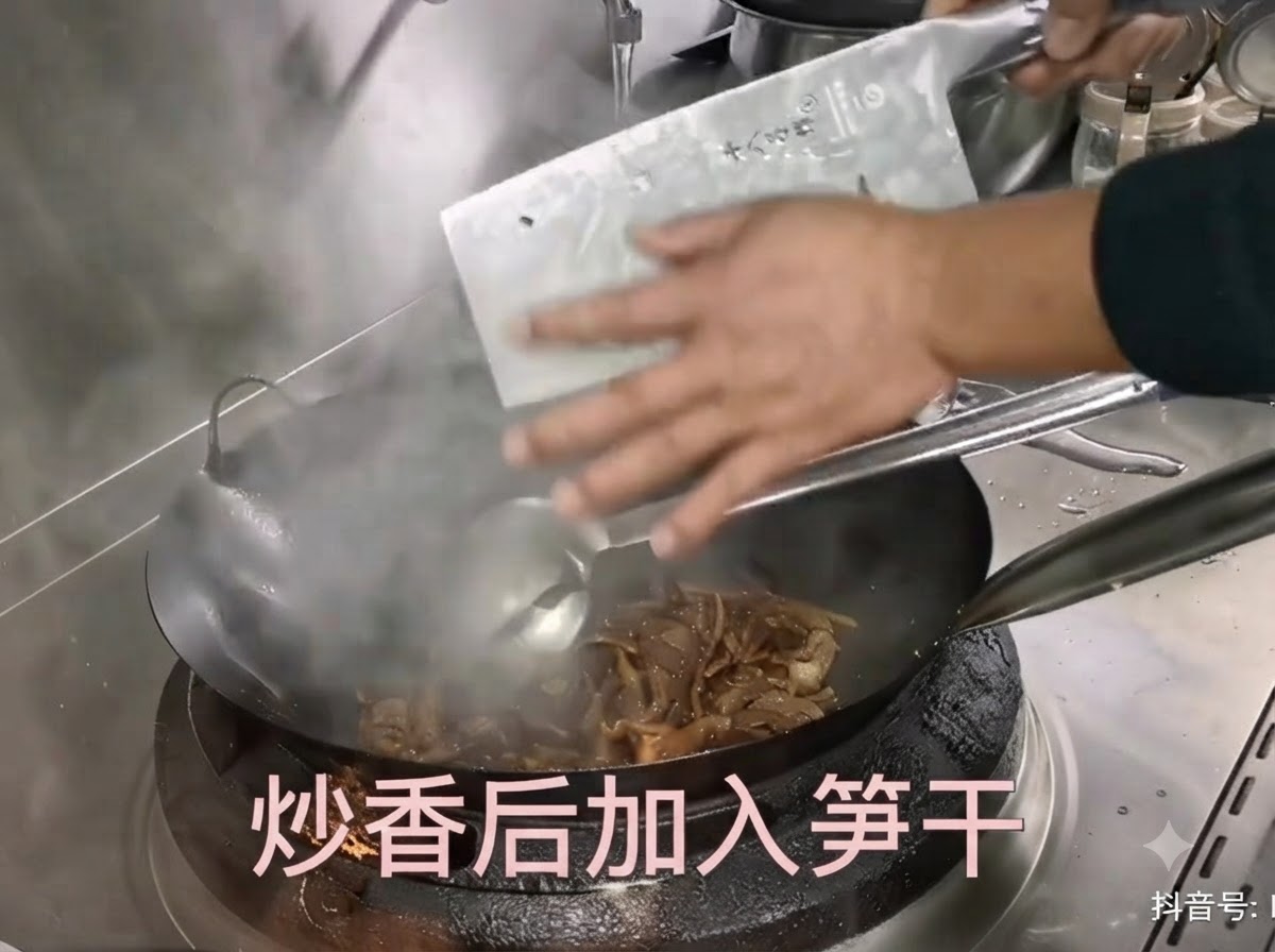 Brotes de bambú seco preparados siendo raspados desde un cuchillo de cocina hacia un wok caliente con cerdo salteado.