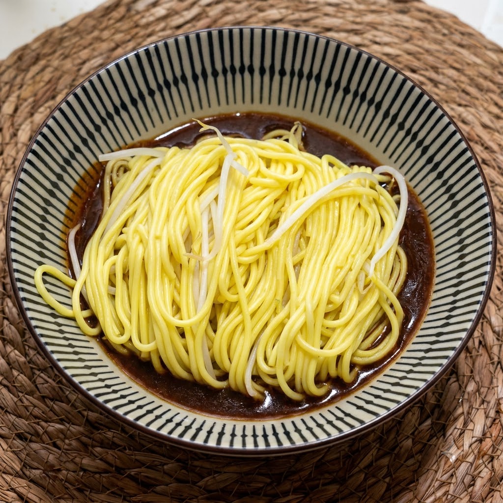 Una porción de fideos amarillos calientes y cocidos reposando en un cuenco de cerámica con motivos sobre una rica salsa marrón oscura.