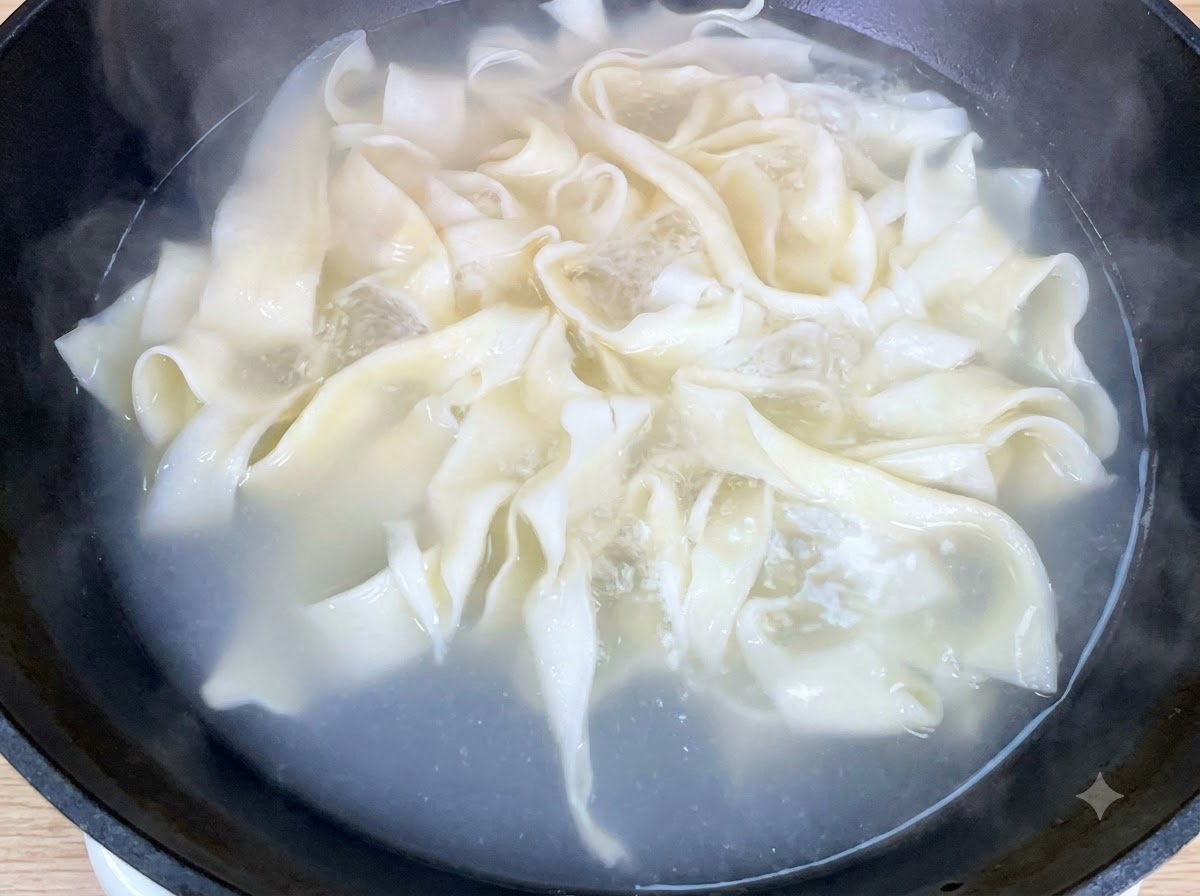 Bok choy tierno fresco hirviendo junto a los fideos anchos en una sartén.