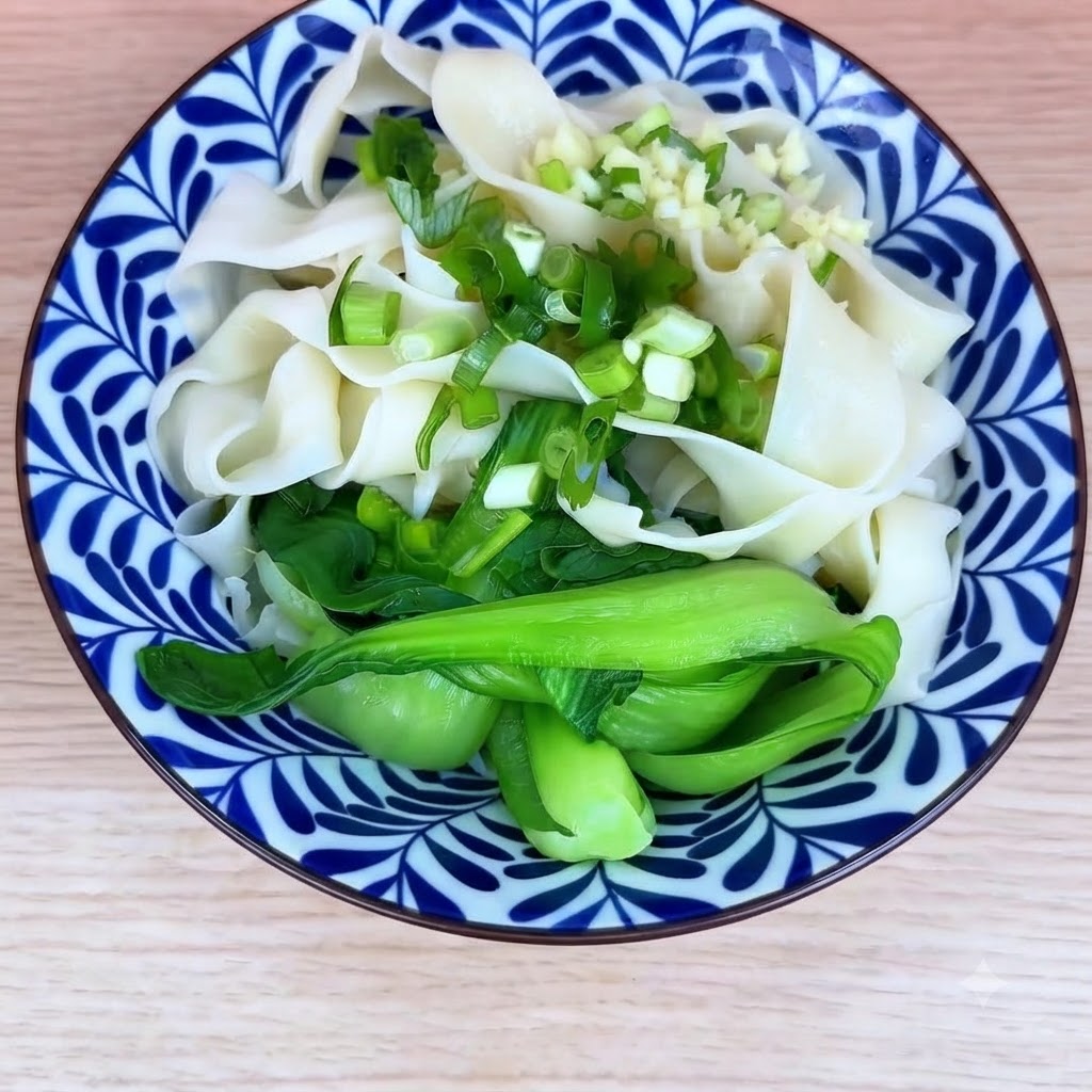 Un tazón de fideos cocidos y bok choy cubierto con cebollino picado y ajo picado.