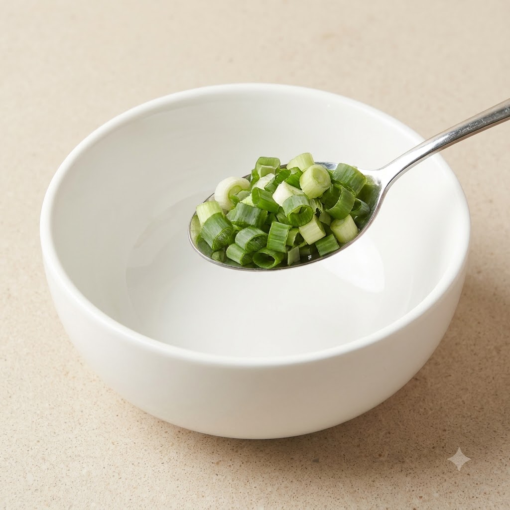 Una cuchara de metal llena de cebolleta verde recién picada sobre un tazón blanco.