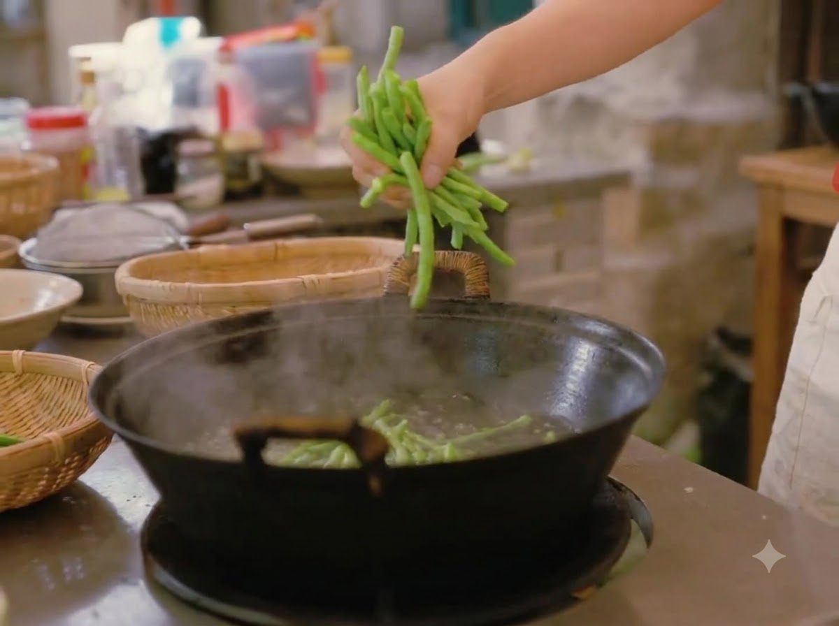 Una mano echando un puñado de judías verdes frescas en un wok grande con agua hirviendo.