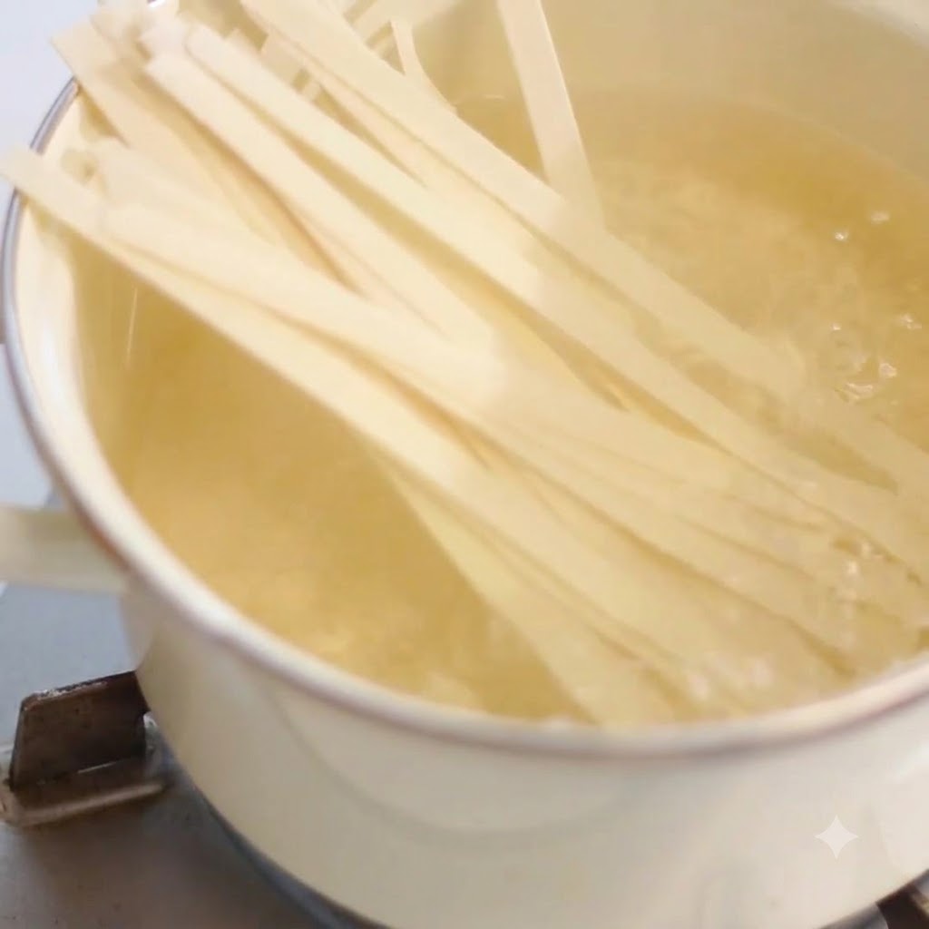 Fideos anchos cociéndose dentro de una olla con agua hirviendo en una estufa.