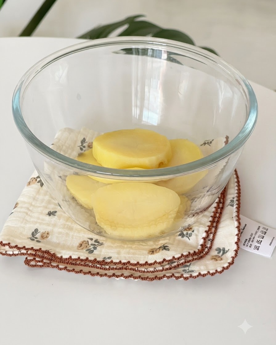 Rodajas de patatas amarillas al vapor reposando dentro de un bol de vidrio transparente sobre un paño.