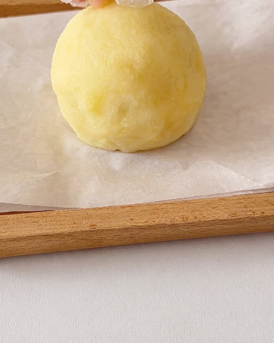 Una bola redonda de puré de patata suave siendo moldeada a mano con pequeños trozos de patata añadidos encima para las orejas.