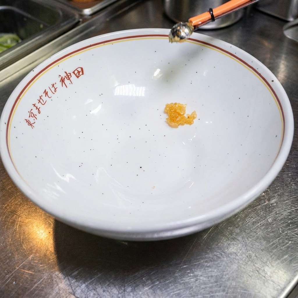 Una pequeña cantidad de líquido sazonado en el fondo de un tazón blanco vacío con texto en japonés.