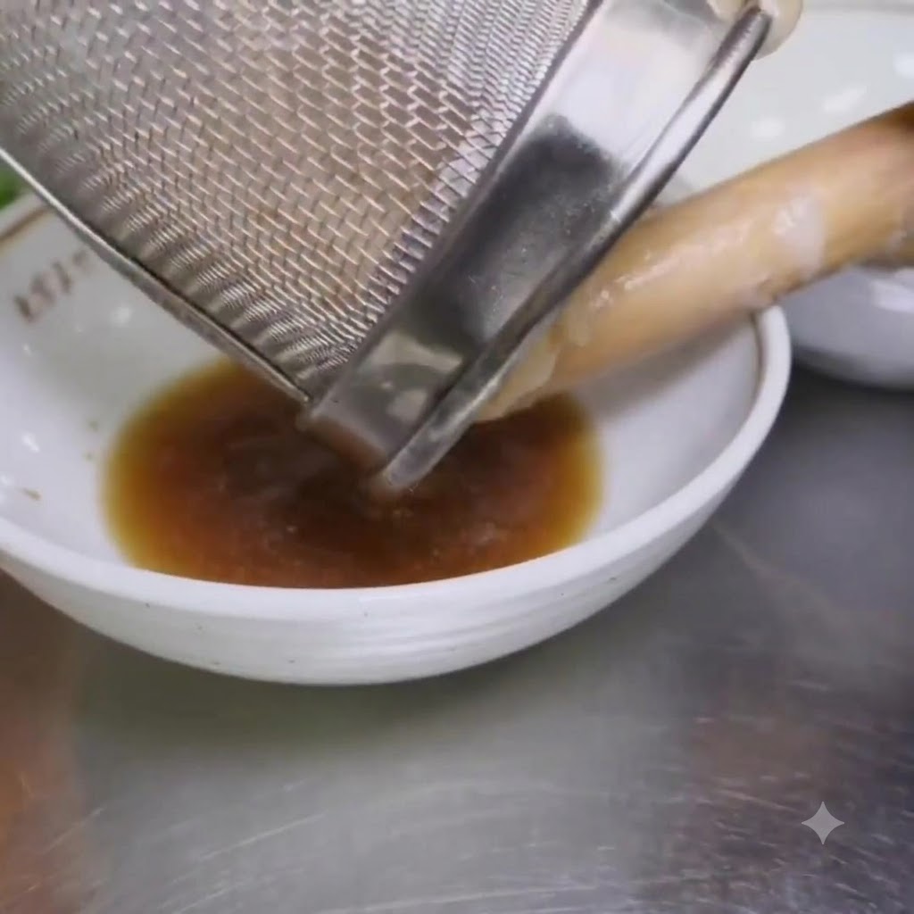 Fideos ramen hervidos siendo vertidos desde un colador de malla en un tazón que contiene condimento.