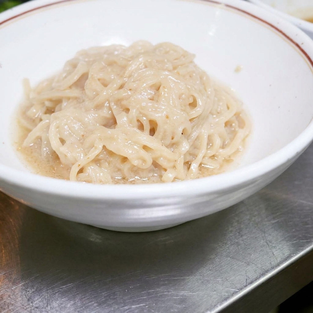 Fideos ramen cocidos ordenadamente dentro de un tazón blanco, listos para ser mezclados con la salsa.