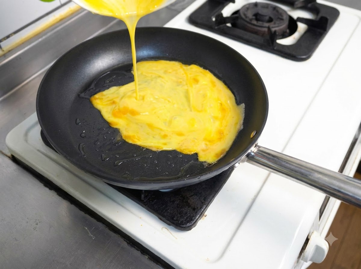 Huevos amarillos batidos siendo vertidos desde un recipiente a una sartén caliente que contiene aceite.