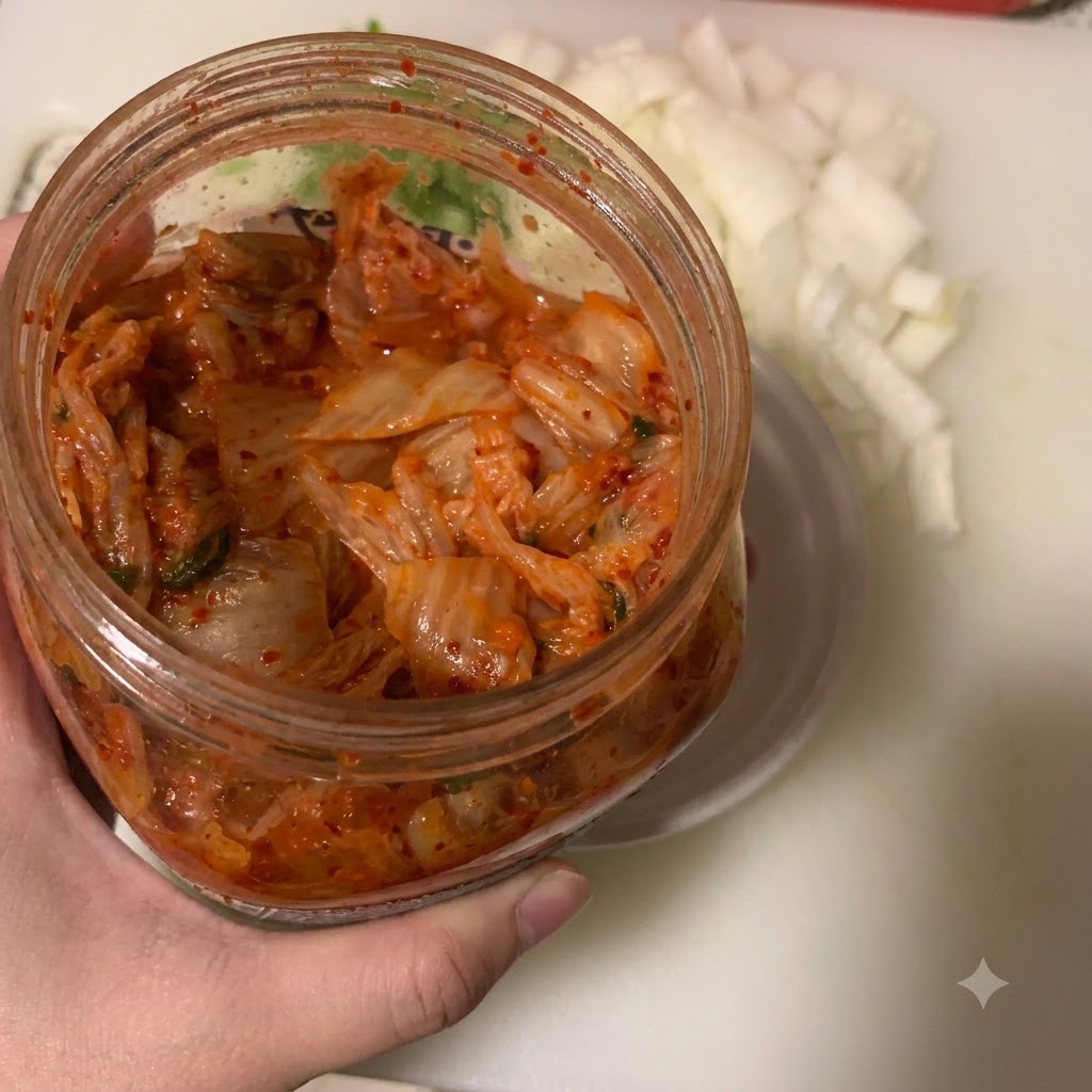 Kimchi siendo transferido con una cuchara a un pequeño cuenco blanco junto a un recipiente con cebolla picada.