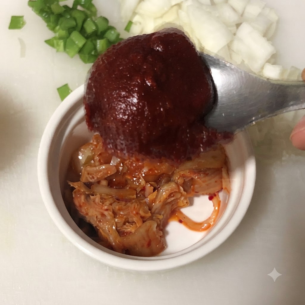 Una cuchara con pasta de ají coreano sobre un cuenco que contiene kimchi picado.