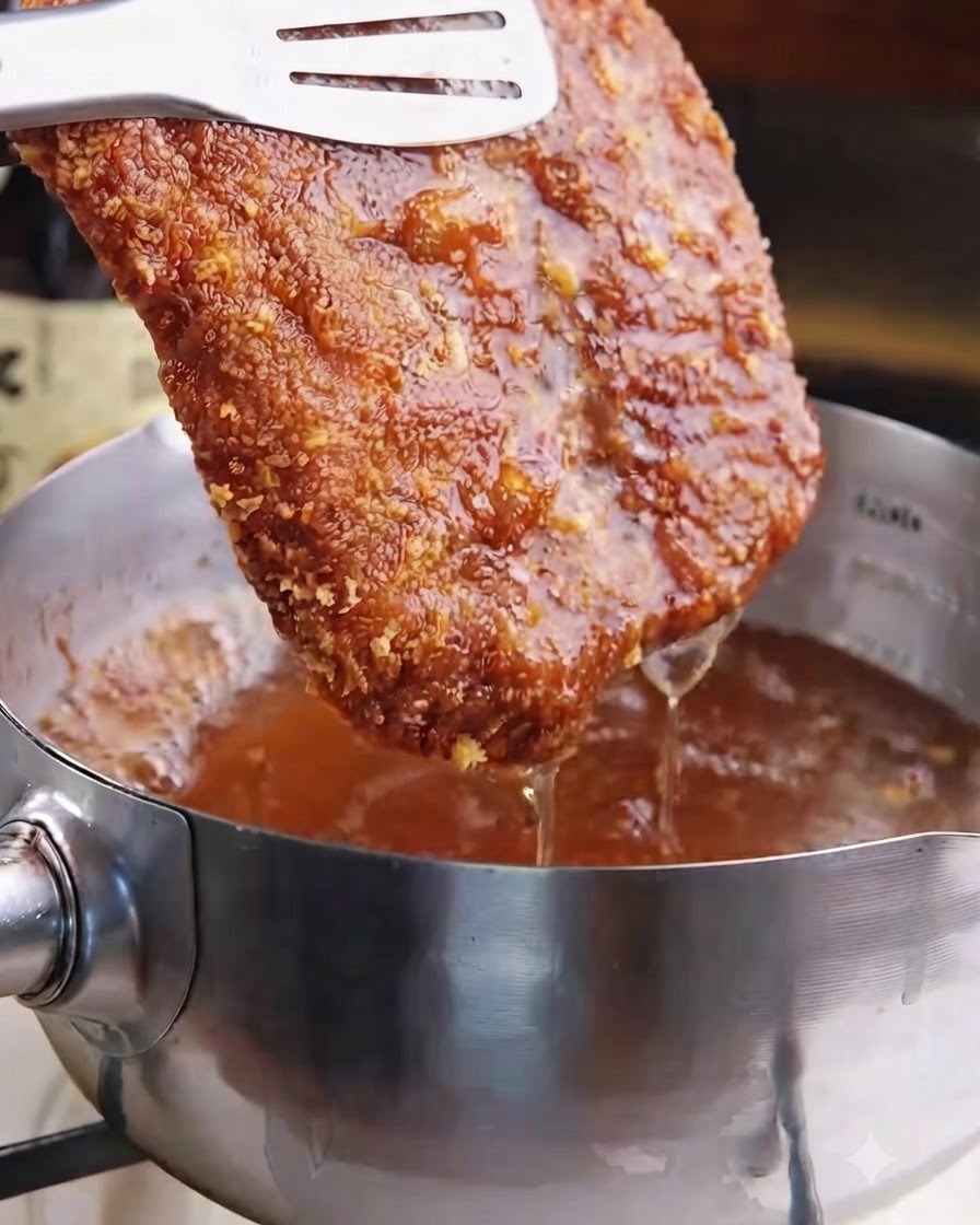 Una chuleta de cerdo frita dorada siendo levantada del aceite caliente con pinzas.
