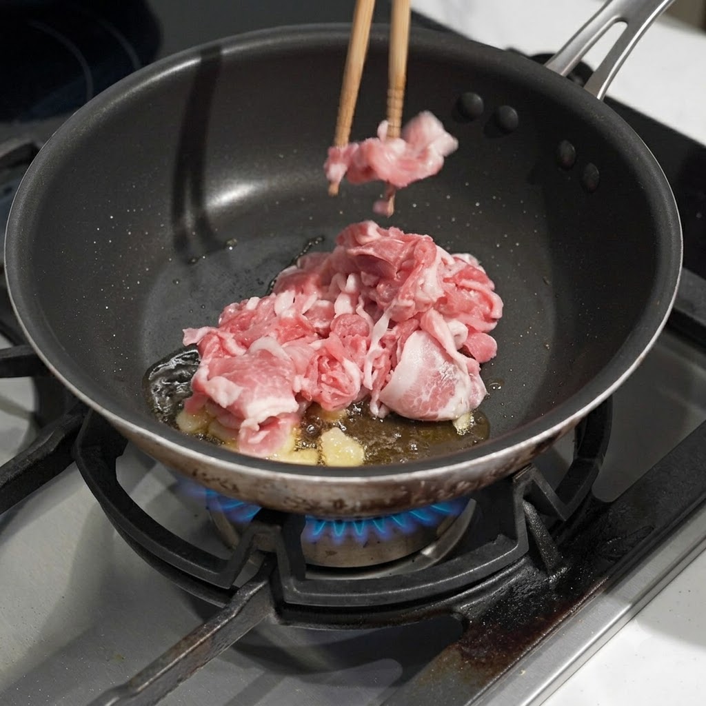 Cerdo crudo cortado finamente siendo colocado en una sartén con aceite caliente y ajo friéndose usando palillos.