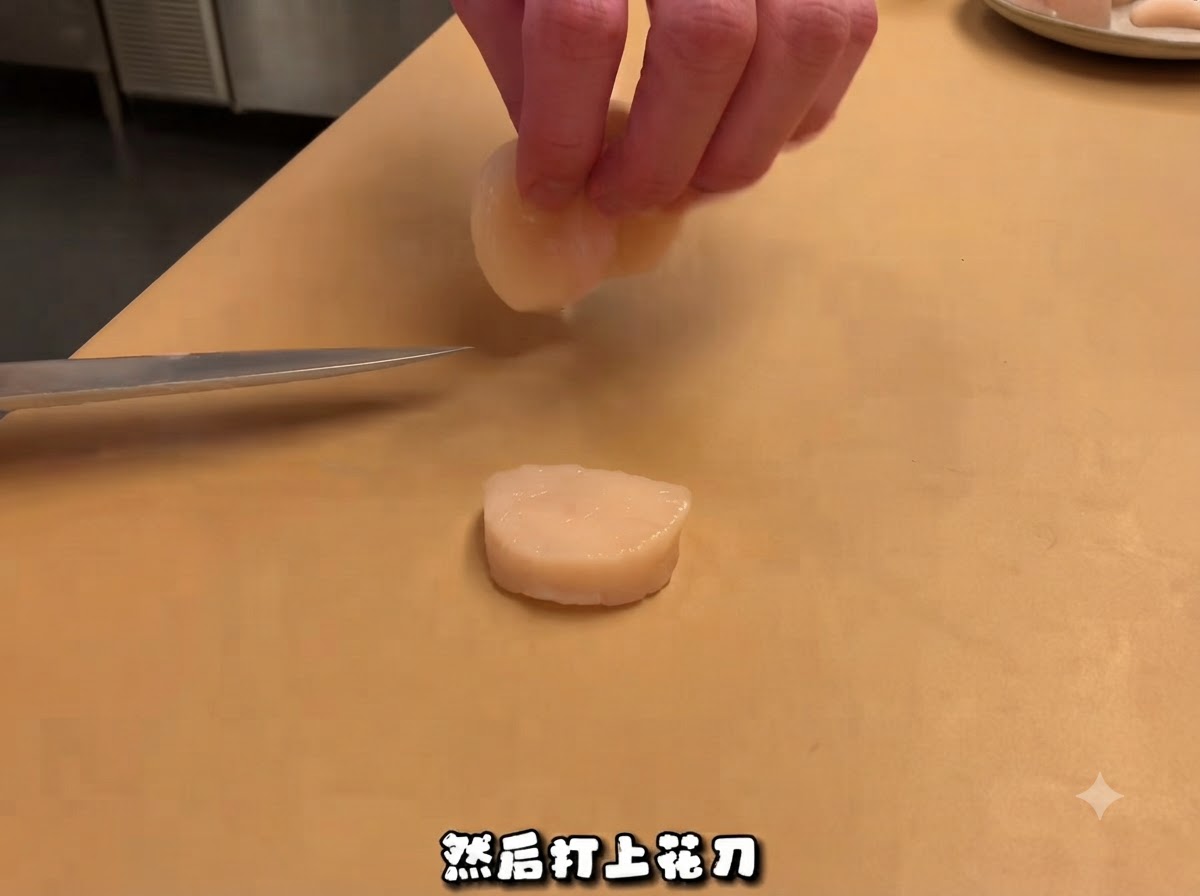 Un cuchillo de chef descansando cerca de una vieira cruda cortada en una tabla de cortar, con manos manipulando una pieza arriba.