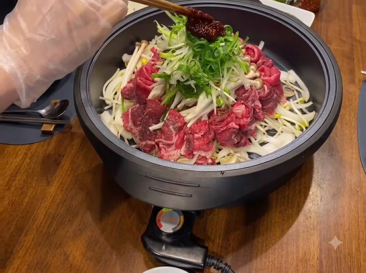Una porción de salsa de condimento de color rojo oscuro colocada encima de cebollas verdes picadas y carnes en una sartén negra.