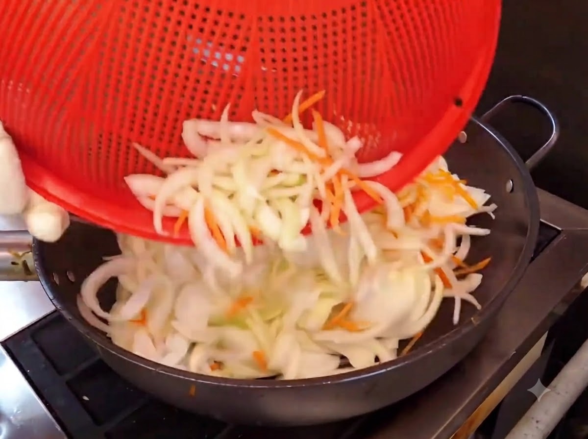 Tiras de cebolla y zanahoria siendo vertidas desde una cesta roja a un wok caliente para saltear.