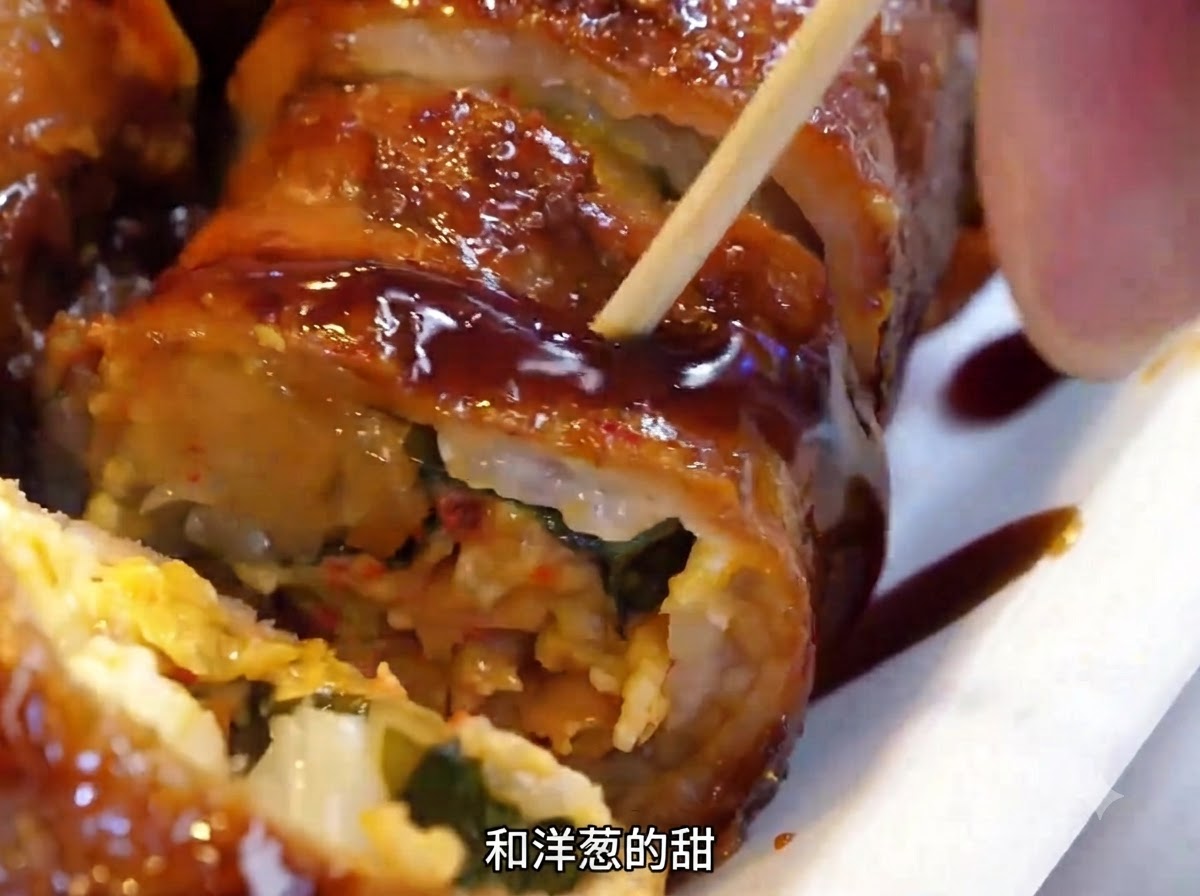 Rollos de carne siendo volteados en la placa de hierro caliente usando una espátula de metal.