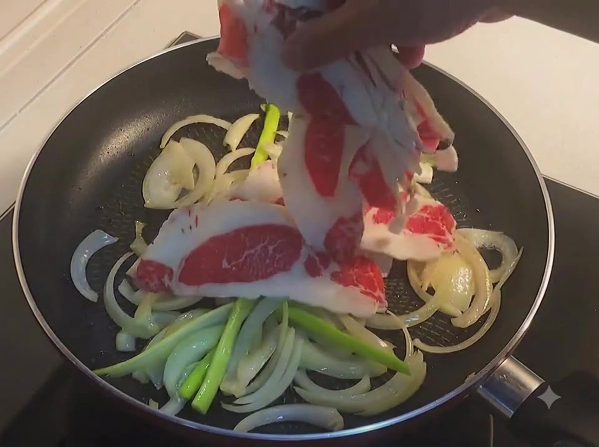 Una mano colocando finas rodajas de panceta de ternera cruda en una sartén con cebollas y cebolletascite: 1.