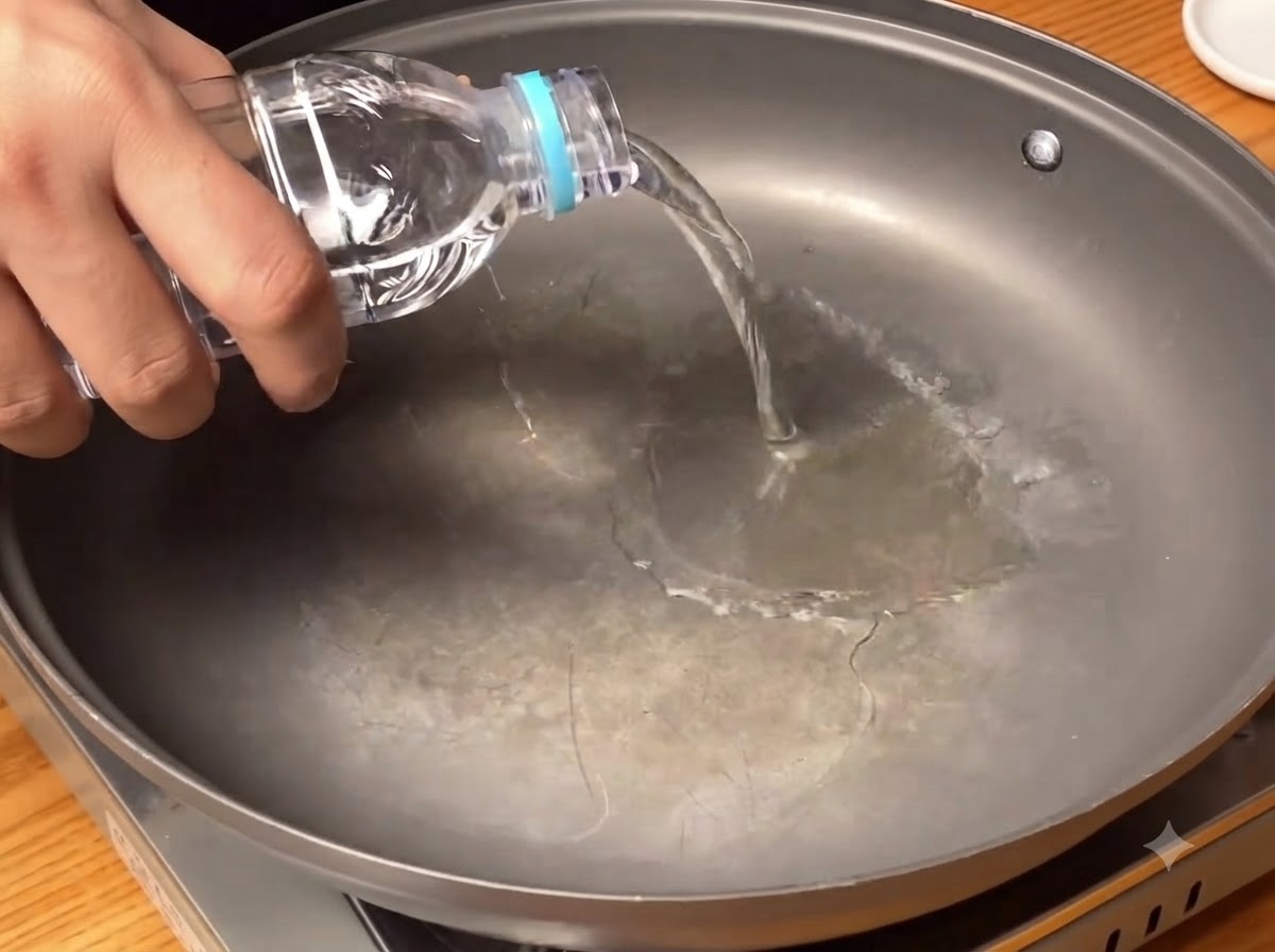 Agua clara siendo vertida desde una botella en el fondo de una sartén ancha.