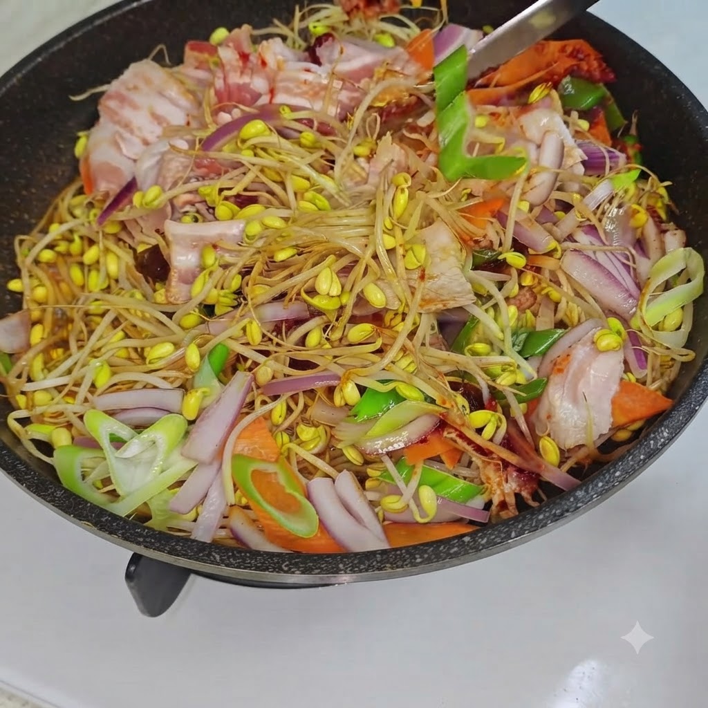 Un utensilio de cocina removiendo los brotes de soja mixtos, la panceta y las verduras dentro de una sartén al fuego.