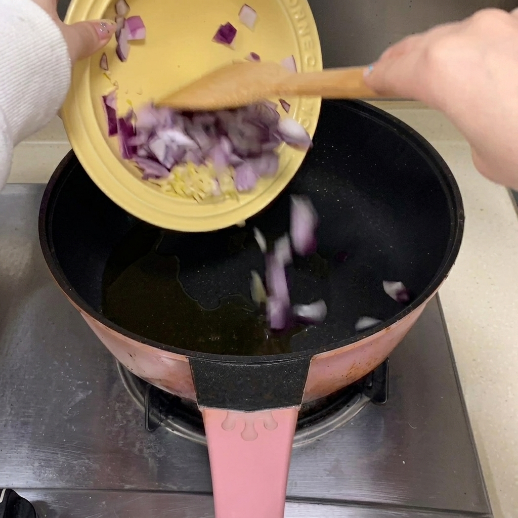 Ajo picado y trozos de cebolla morada cayendo en una sartén con aceite caliente.