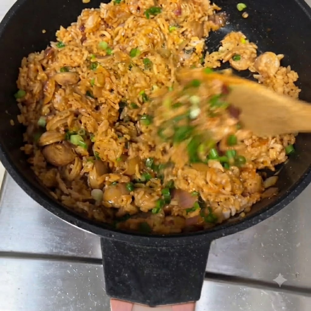 Arroz frito siendo revuelto con una espátula de madera en una sartén, adornado con cebollitas de verdeo.