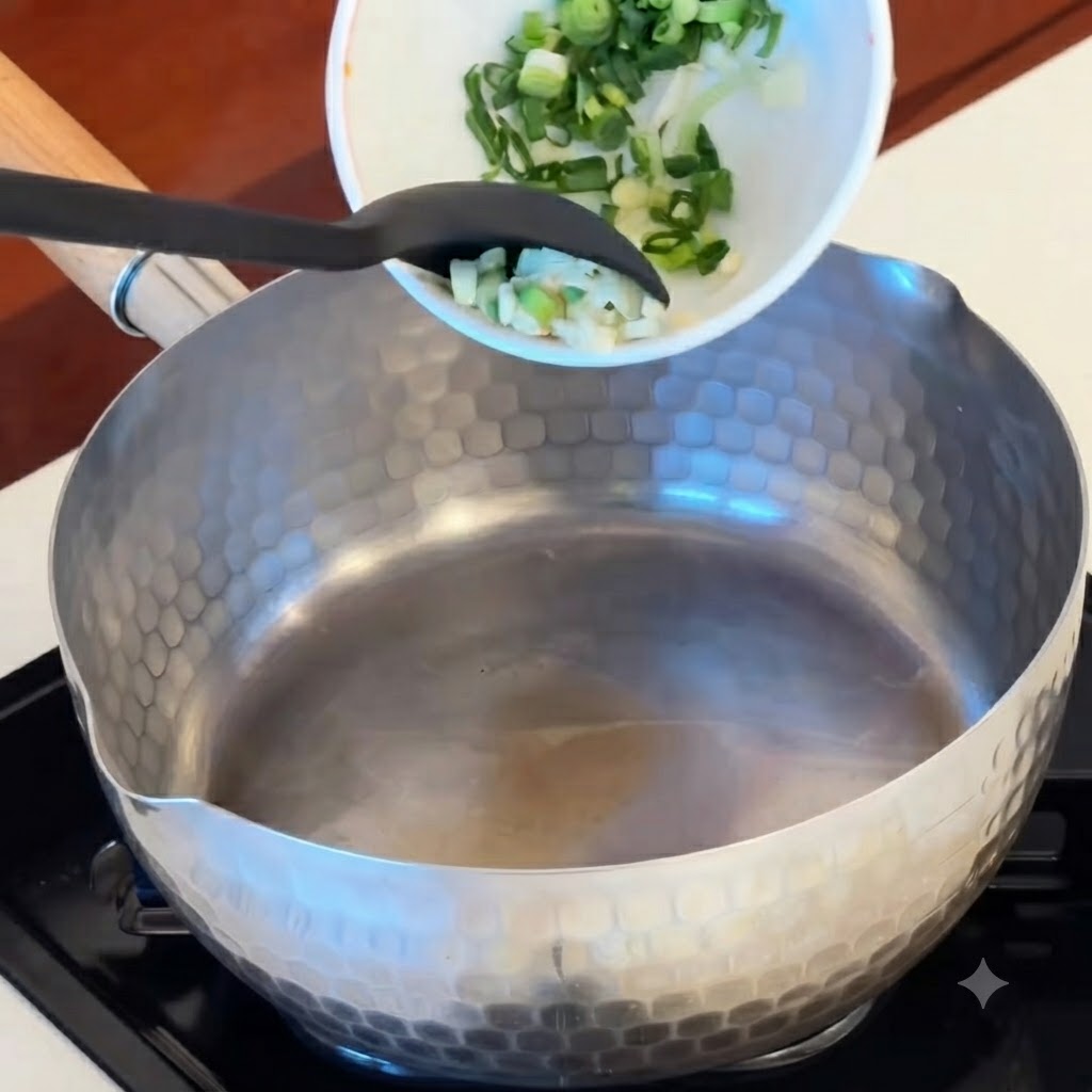 Ajo en rodajas, trozos de kimchi rojo y rodajas de salchicha siendo vertidos desde un tazón hacia una olla caliente.