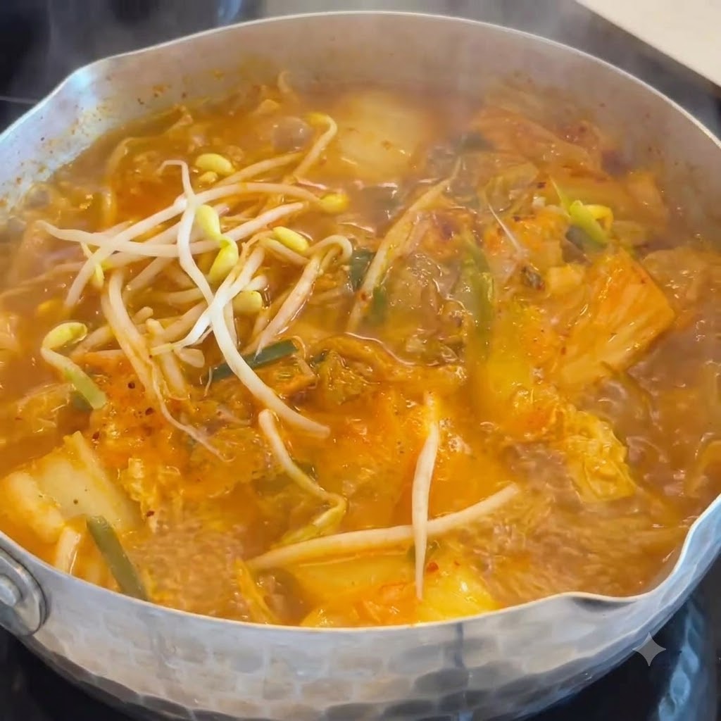Brotes de soja blancos y crujientes siendo arrojados a una olla humeante de sopa de kimchi y salchicha de color naranja.
