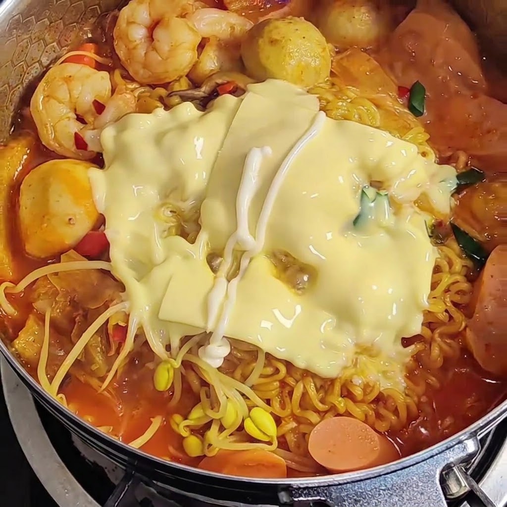 Mayonesa siendo rociada en patrón de zigzag sobre el queso derretido encima del ramen.