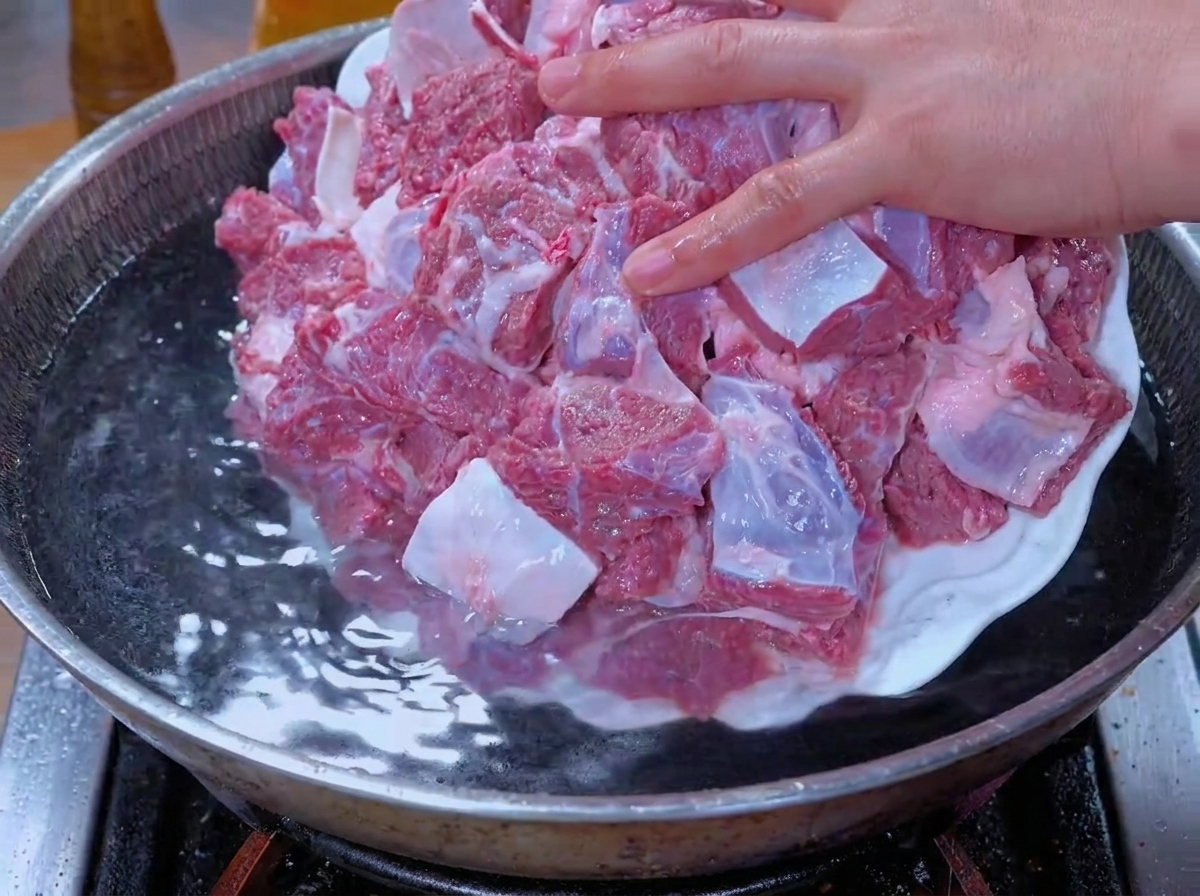 Trozos de carne remojados siendo agregados a una olla con agua para blanquear.