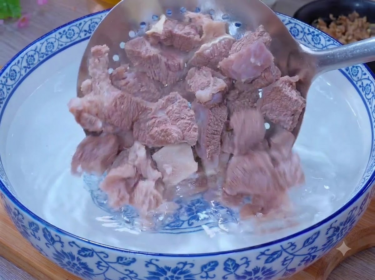 Piezas de carne blanqueadas siendo limpiadas dentro de un tazón de agua tibia usando una cuchara ranurada.
