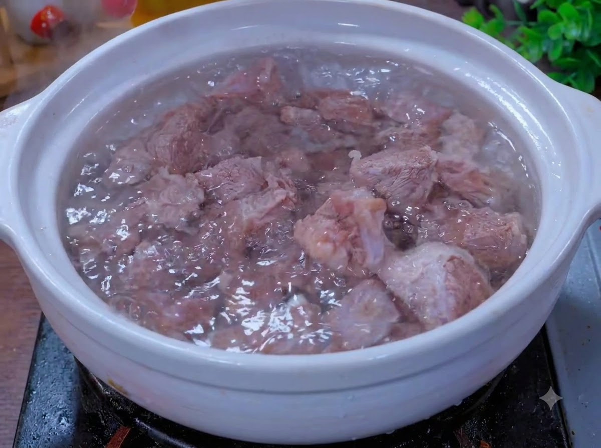 Piezas de carne hirviendo a fuego lento en una olla de barro blanca con aromáticos.