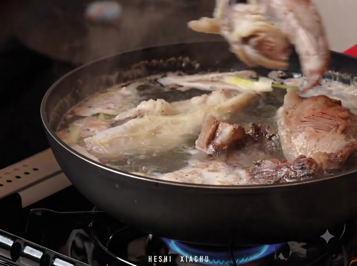 Trozos de pecho de ternera siendo trasladados a una olla con agua caliente, caldo de sopa y aromáticos.