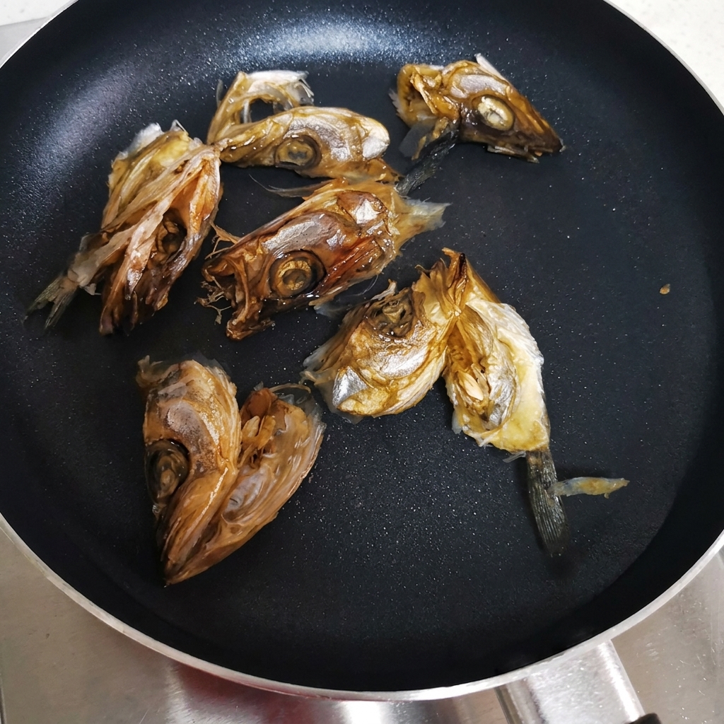 Cabezas de pescado seco dispuestas en una sartén plana con agua fría listas para ser calentadas.