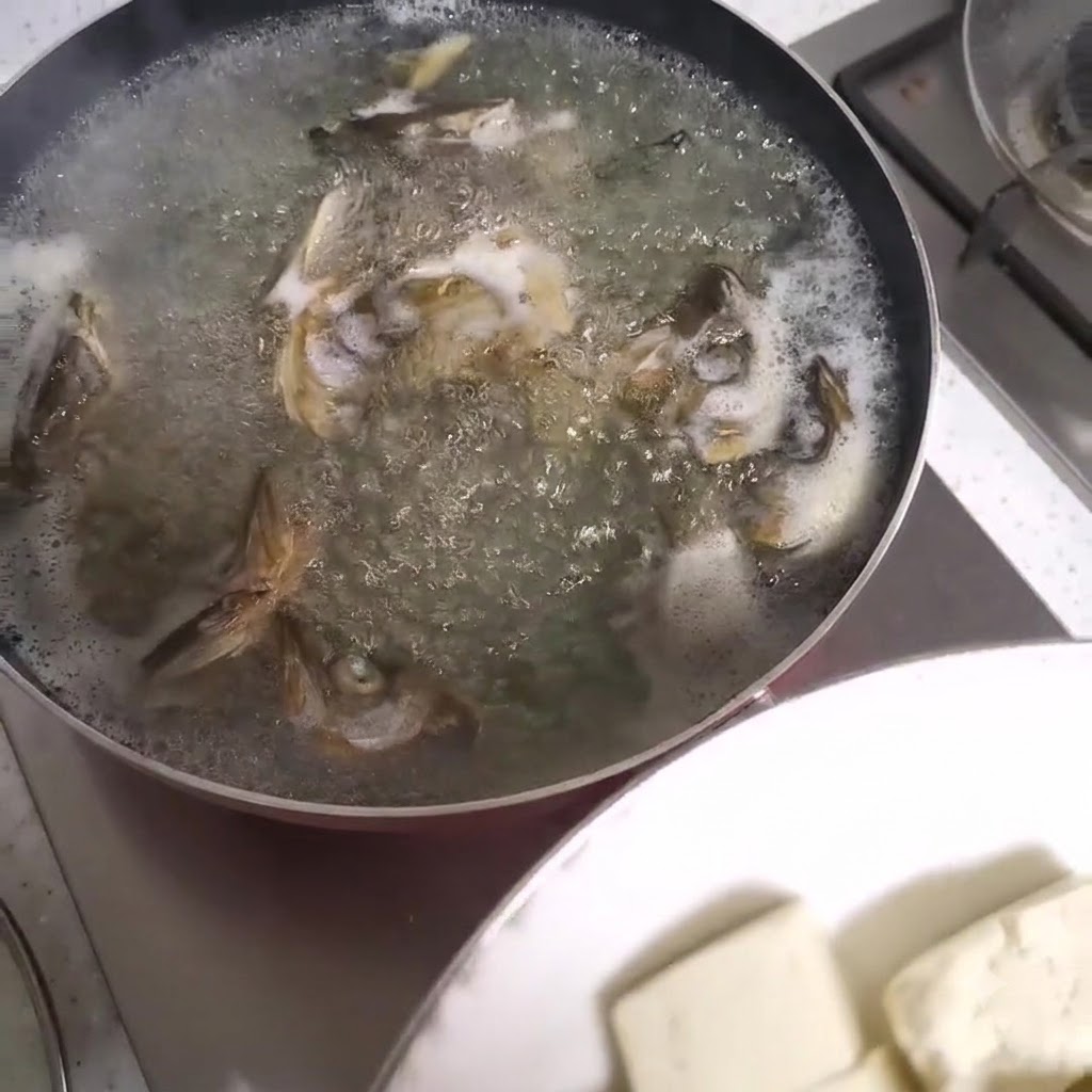 Cubos de tofu siendo añadidos a una olla hirviendo de sopa de cabeza de pescado.